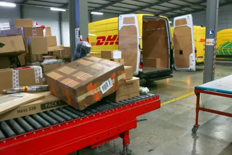 AFP via Getty Images Boxes covered in tape and shipping labels are piled up in a DHL shipping facility.